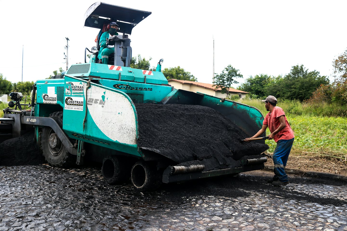 Construction workers pave a road with an asphalt paver.