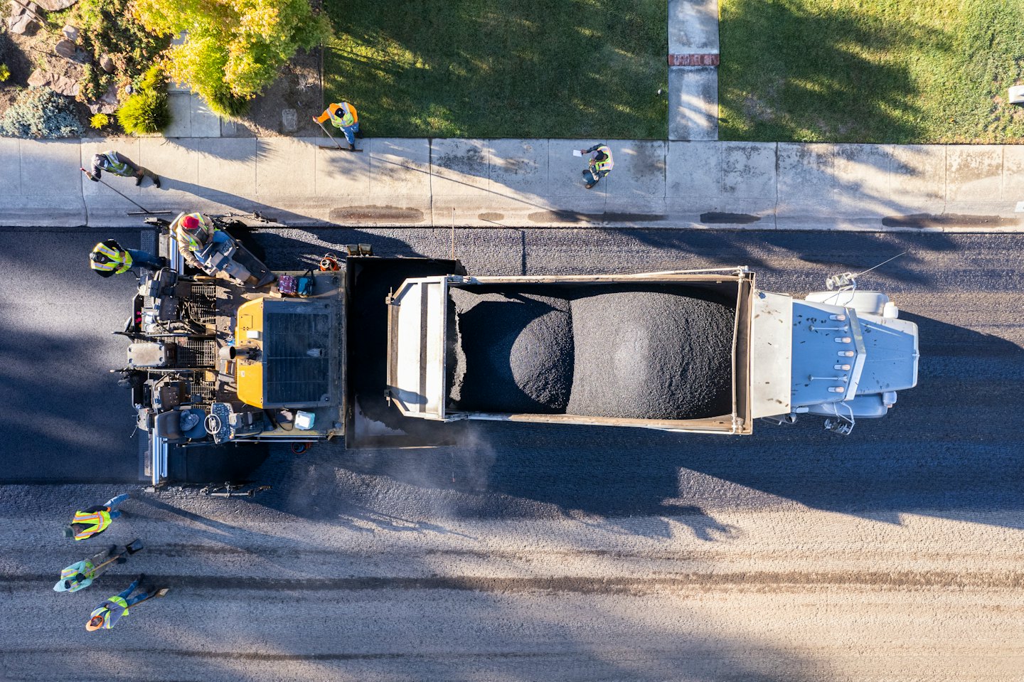 Construction workers use a paving machine to lay fresh asphalt.